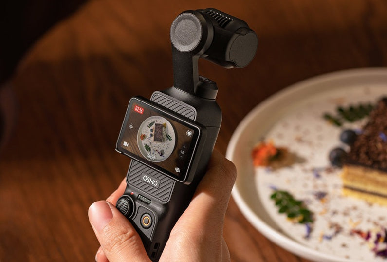 Hand holding a DJI Osmo 3 Pocket Camera device with a blurred plate of food in the background